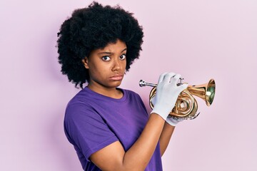 Young african american woman playing trumpet skeptic and nervous, frowning upset because of...