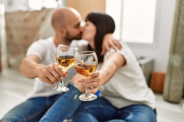 Young hispanic couple kissing and toasting with champagne at new home.