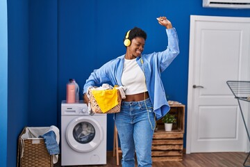 African american woman holding basket with clothes listening to music at laundry room