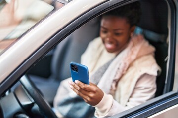 African american woman using smartphone sitting on car at street