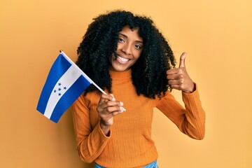 African american woman with afro hair holding honduras flag smiling happy and positive, thumb up...