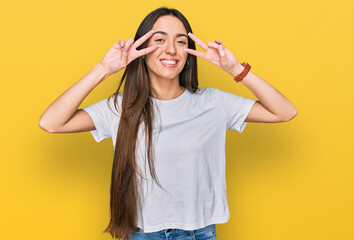 Obraz na płótnie Canvas Young hispanic girl wearing casual white t shirt doing peace symbol with fingers over face, smiling cheerful showing victory