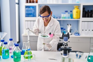 Fototapeta premium Middle age woman wearing scientist uniform looking herb with loupe at laboratory