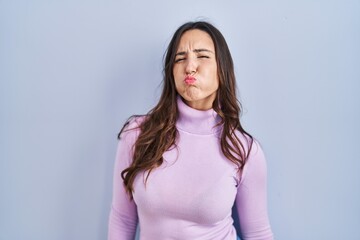 Young brunette woman standing over blue background puffing cheeks with funny face. mouth inflated with air, crazy expression.