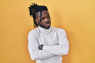 Obraz premium African man with dreadlocks wearing turtleneck sweater over yellow background looking to the side with arms crossed convinced and confident