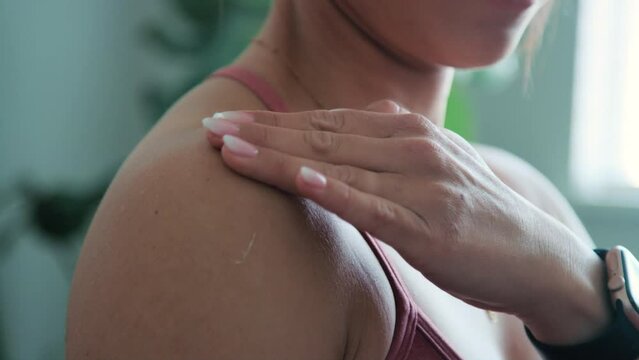 Athletic woman rubs ointment lotion into shoulder as camera wraps around