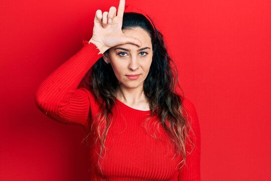 Young hispanic woman wearing casual clothes making fun of people with fingers on forehead doing loser gesture mocking and insulting.