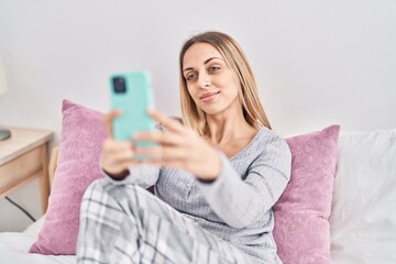 Young woman make selfie by the smartphone sitting on bed at bedroom