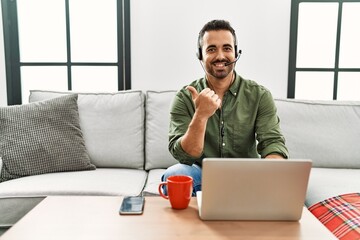 Young hispanic man with beard wearing call center agent headset working from home pointing to the...