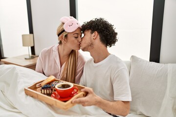 Young beautiful couple having breakfast on the bed at home.