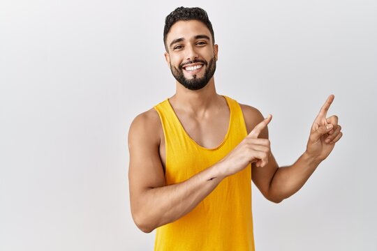 Young handsome man with beard standing over isolated background smiling and looking at the camera pointing with two hands and fingers to the side.