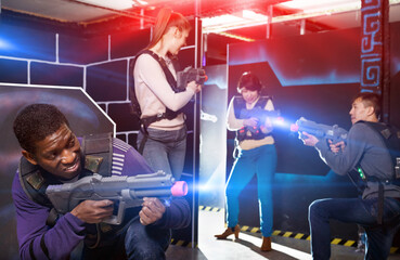 Fototapeta premium Emotional African man with a laser pistol playing laser tag with friends at the dark labyrinth