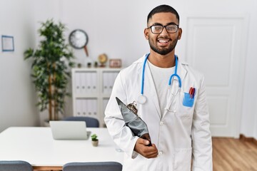 Young indian man wearing doctor uniform and stethoscope winking looking at the camera with sexy...