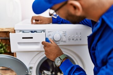 Obraz premium Young arab man wearing technician uniform repairing washing machine at laundry room