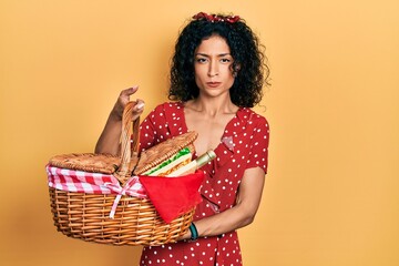 Young latin girl holding picnic wicker basket with bread skeptic and nervous, frowning upset because of problem. negative person.