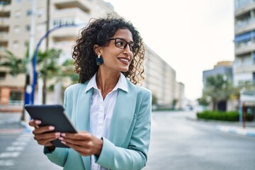 Young hispanic business woman wearing professional look smiling confident at the city using touchpad device