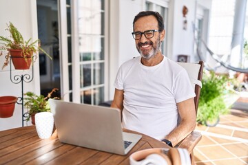 Middle age man using computer laptop at home winking looking at the camera with sexy expression,...