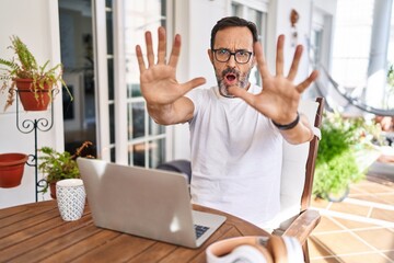 Middle age man using computer laptop at home doing stop gesture with hands palms, angry and...