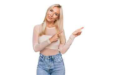 Young blonde woman wearing casual clothes smiling and looking at the camera pointing with two hands and fingers to the side.