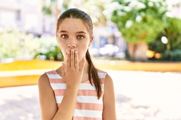 Young teenager girl outdoors on a sunny day covering mouth with hand, shocked and afraid for...