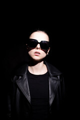 woman in leather coat and black sunglasses, black background