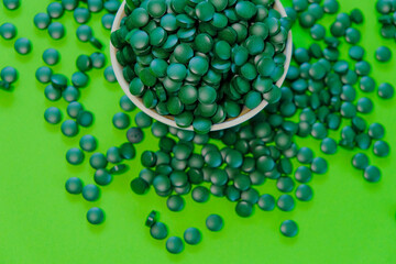 Spirulina pills in a round green bowl.Green spirulina tablets on green background. Vitamins and dietary supplements 