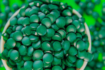 Spirulina tablets.Spirulina pills in a round green bowl. spirulina tablets on green background. Vitamins and dietary supplements 