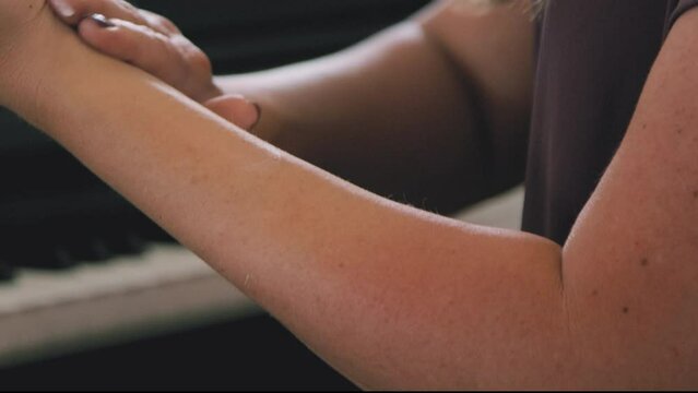 Woman rubs pain relief cream into forearm while sitting next to piano
