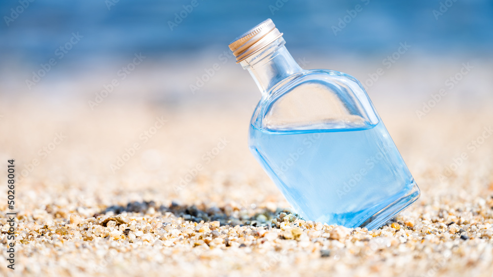 Wall mural a glass bottle of blue water on the beach on sunny day, tropical summer vacation background