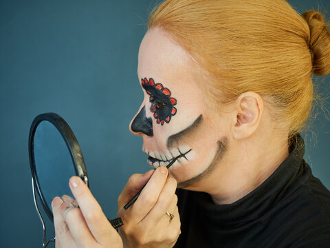 Mature woman in black turtleneck doing scary makeup for halloween holiday looking in the mirror