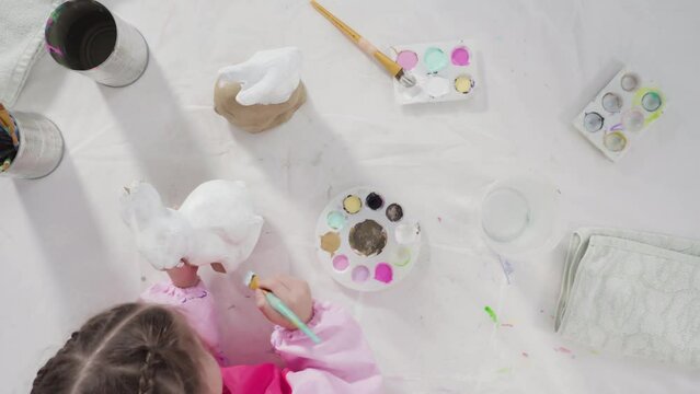 Time lapse. Flat lay. Little girl painting paper mache figurine at homeschooling art class.