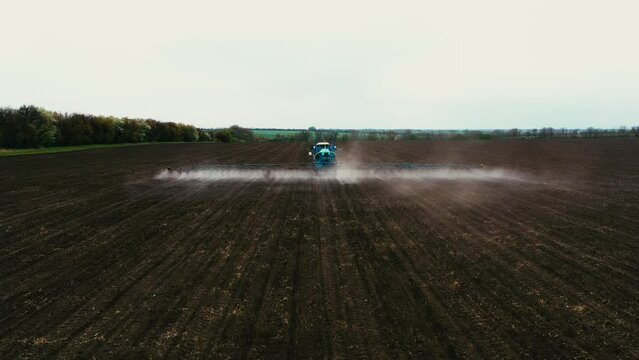 Aerial view of farming tractor spraying on field with sprayer, herbicides and pesticides at sunset. Farm machinery spraying insecticide to the green field, agricultural natural seasonal spring works.