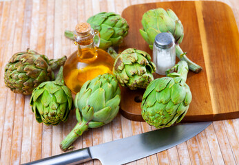Raw ripe green artichokes, salt and olive oil on wooden table, ingredients for cooking at home