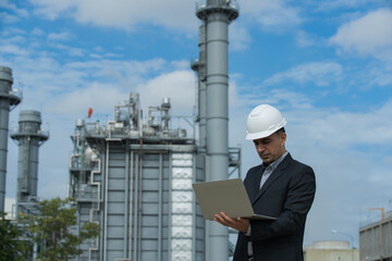 Engineers male in suite working with laptop  at power plant. Energy power station area with sky, sunset. Concept safety,industry