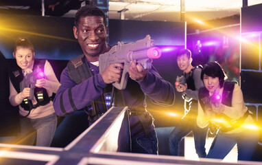 Portrait of cheerful positive smiling African-American with laser gun having fun on dark laser tag arena