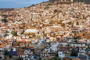 Fototapeta na wymiar The city is illuminated by the sun in the morning on a mountainside with colonial architecture, many white houses with tiles. The cramped streets of Taxco in Mexico