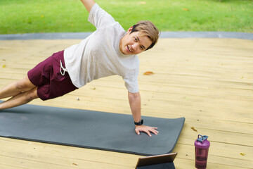 Active sportsman doing a side plank exercise and making a video call with a friend and online sport training coach. Healthy sport man making a body building workout with online instructor.