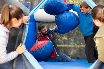 Two cheerful men having funny battle by big boxing gloves on inflatable arena at amusement park