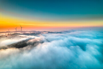 Aerial view top hill at dawn with fog covering small village in valley, beautiful wind power poles rising high to welcome a peaceful new day in highlands Da Lat, Vietnam