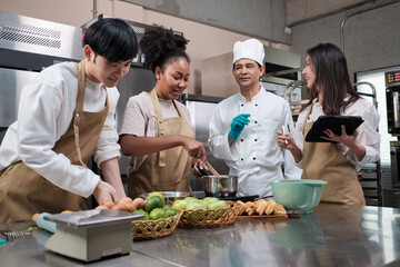 Hobby cuisine course, senior male chef in cook uniform teaches young cooking class students to...