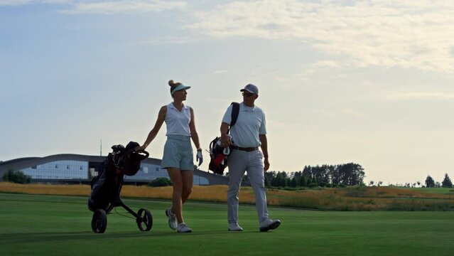 Couple golf players discuss sport course outside. Two golfers walk grass field.