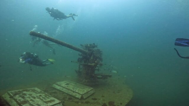 Under water scuba diving film - The large gun torrent of the ship wreck HTMS Sattakut - flanked by divers - Southern Thailand