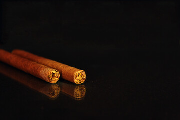 Two cigarillos on a black mirror background close-up