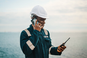 Black seaman with walkie talkie speaking on smartphone