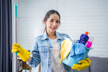 Happy woman wearing white shirt and denim shirt She wears yellow protective gloves, carries a mop...