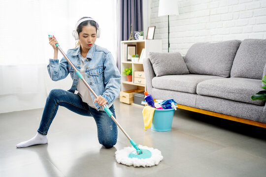 Beautiful Asian housewife enjoys cleaning the house. She is listening to her favorite music with wireless headphones.