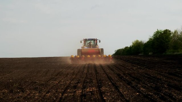 A modern tractor with sows a field. . A farmer on a tractor plows dusty arid soil and sows cereal grains. Agribusiness in the spring. Agricultural work in the fields, agribusiness. Selective focusing