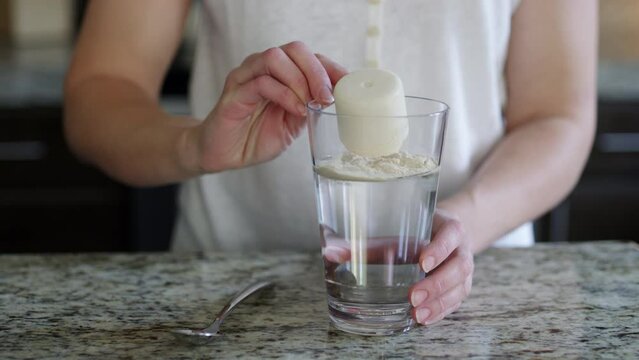 Woman pours a scoop of vanilla protein powder into a glass and stirs