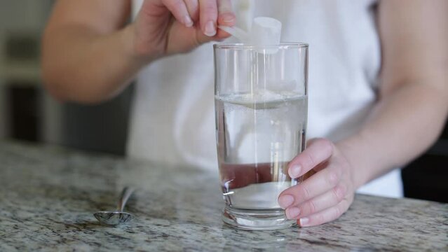 Energy drink powder is poured into clear glass and stirred, turning yellow