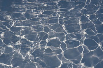 Blue water surface with bright sun light reflections in swimming pool background